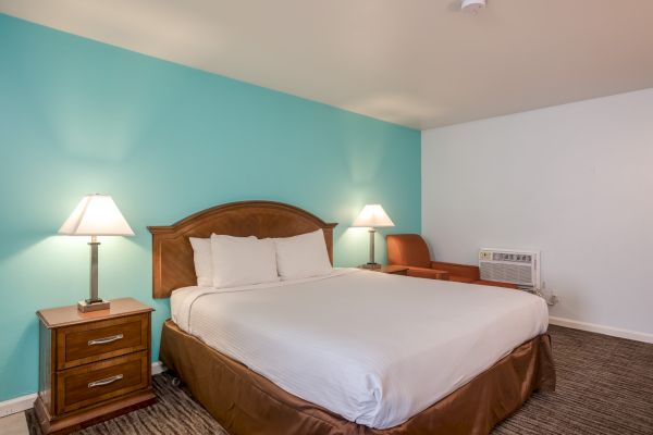 A neatly arranged hotel room with a double bed, two bedside tables with lamps, an armchair, and a teal accent wall.