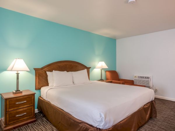 A neatly arranged hotel room with a double bed, two bedside tables with lamps, an armchair, and a teal accent wall.