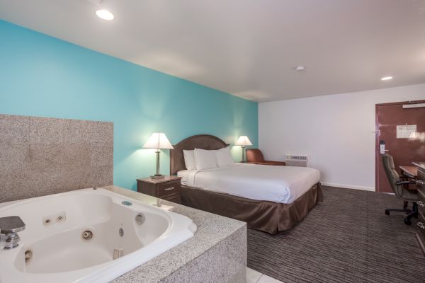 A hotel room with a bed, bedside tables, lamps, a desk, chair, and a jacuzzi tub.