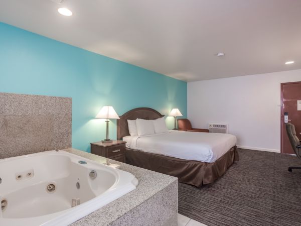 A hotel room with a bed, bedside tables, lamps, a desk, chair, and a jacuzzi tub.