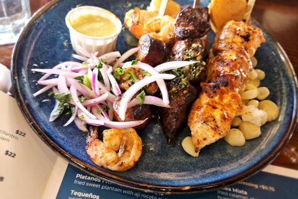 The image shows a plate of skewers with chicken and beef, garnished with onions and sauce, accompanied by shrimp and corn.