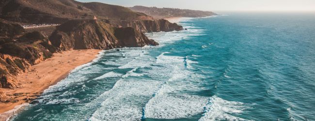 A scenic coastline with cliffs, sandy beaches, and ocean waves under a bright blue sky.