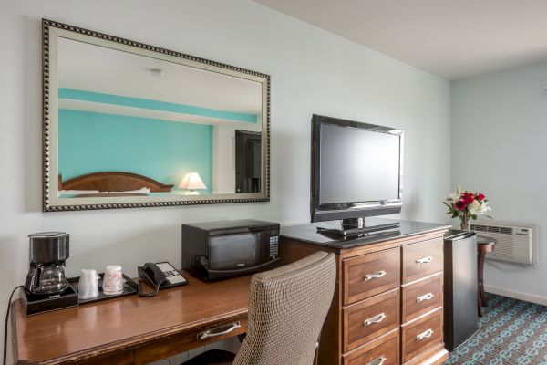 A hotel room desk with a mirror, TV, microwave, coffee maker, chair, lamp, and flowers.