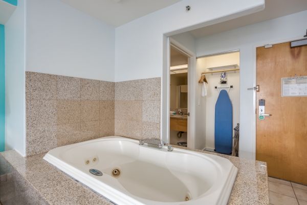 The image shows a bathroom with a whirlpool bathtub, granite tiles, and an ironing board near the entrance of a hotel room.