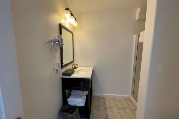 A bathroom with a black vanity, mirror, wall-mounted hair dryer, tiled floor, and a glass shower enclosure.