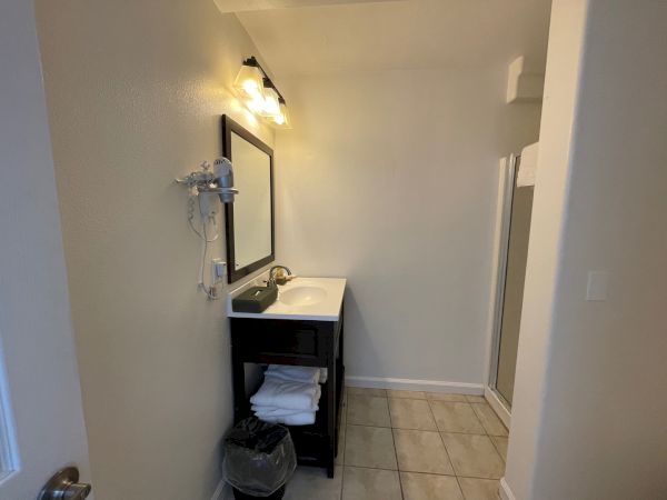 A bathroom with a black vanity, mirror, wall-mounted hair dryer, tiled floor, and a glass shower enclosure.