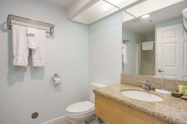 A bathroom features a sink, toilet, mirror, towel rack with towels, toilet paper holder, and a closed door.