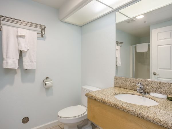A bathroom features a sink, toilet, mirror, towel rack with towels, toilet paper holder, and a closed door.