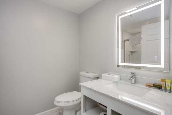 A modern bathroom with a toilet, a sink with a marble countertop, and an illuminated mirror above the sink.