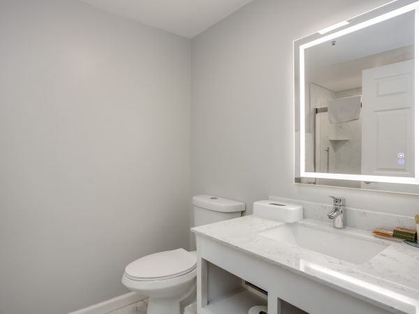 A modern bathroom with a toilet, a sink with a marble countertop, and an illuminated mirror above the sink.