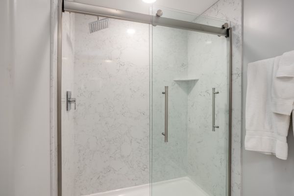 A modern shower with sliding glass doors, marble walls, and a towel hanging on the right side.