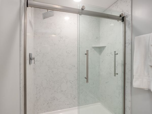 A modern shower with sliding glass doors, marble walls, and a towel hanging on the right side.