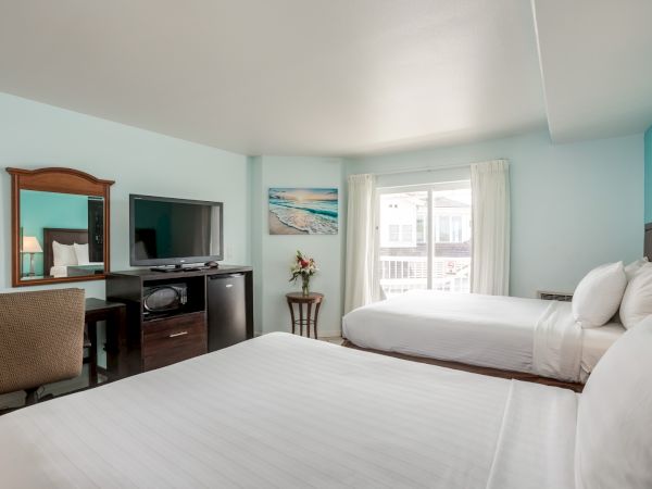 A hotel room with two beds, a TV, desk with chair, and a window showing an outdoor view, decorated in a light, airy style.