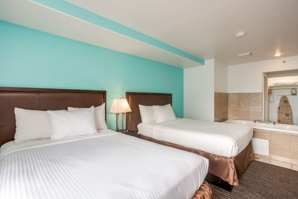 The image shows a hotel room with two beds, a nightstand with a lamp, and a whirlpool tub in the background.