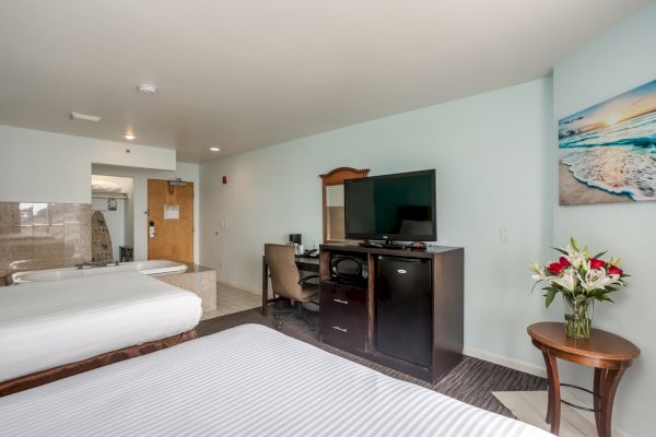 The image shows a hotel room with two beds, a TV, a desk, and a flower vase on a side table. There's a bathroom entrance visible.