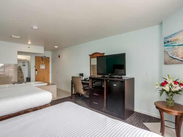 The image shows a hotel room with two beds, a TV, a desk, and a flower vase on a side table. There's a bathroom entrance visible.