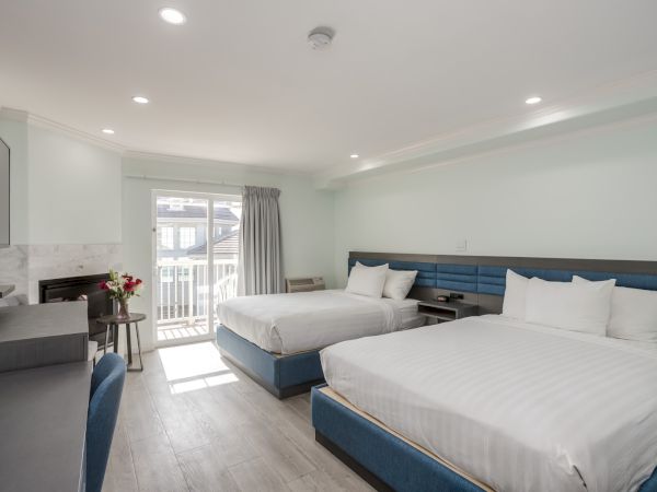 A hotel room with two double beds, a small table with flowers, a TV, and a balcony door. Bright and minimalist decor completes the look.