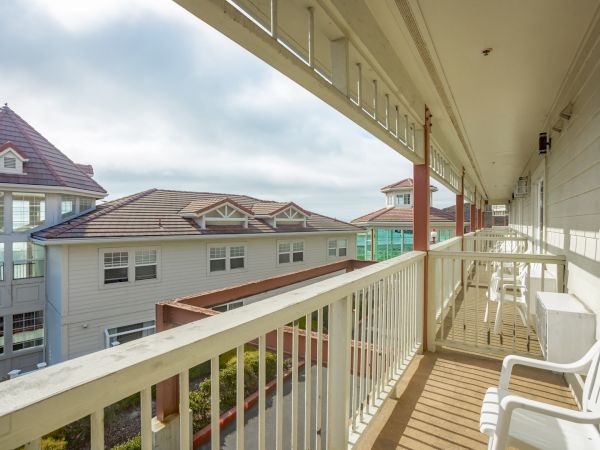 A balcony with white railings and chairs overlooks neighboring buildings with tiled roofs under a partly cloudy sky.