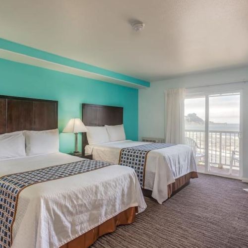 A hotel room with two beds, lamps, a turquoise accent wall, and a sliding glass door leading to a balcony with a view.