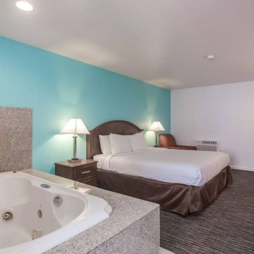 A hotel room with a bed, lamps, a desk, and a whirlpool tub in the foreground. The walls are painted blue and white.