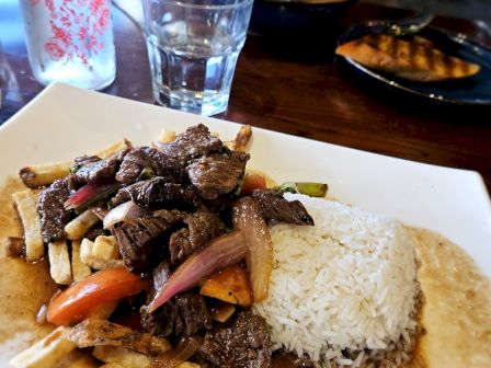 A dish featuring stir-fried beef, onions, and vegetables with rice, likely a Lomo Saltado, alongside a glass of water.